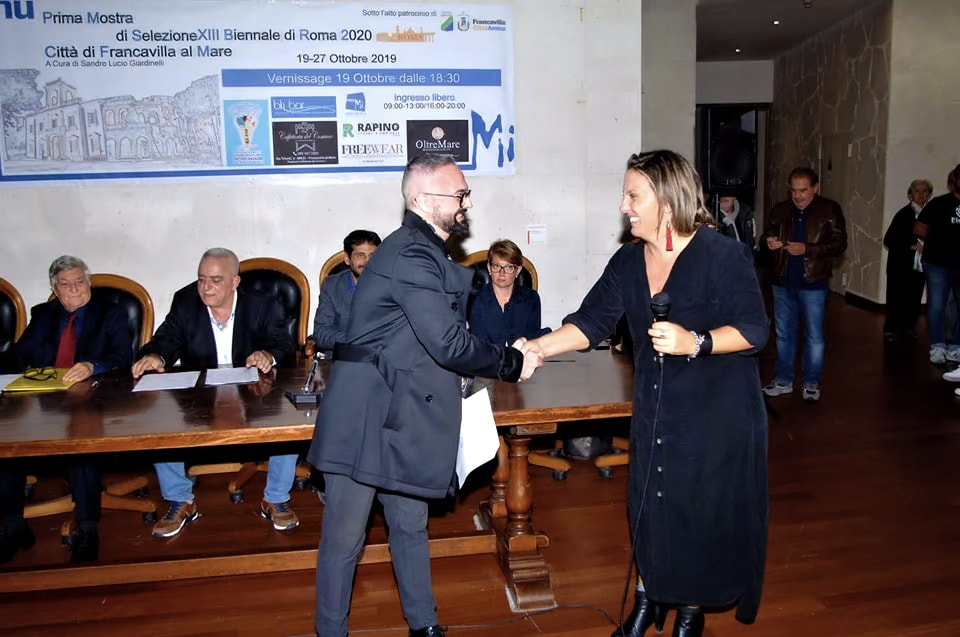 L’une des organisatrices de l’exposition serre la main de Davide Cristofaro à la remise de sa sélection pour la XIIIe Biennale di Roma