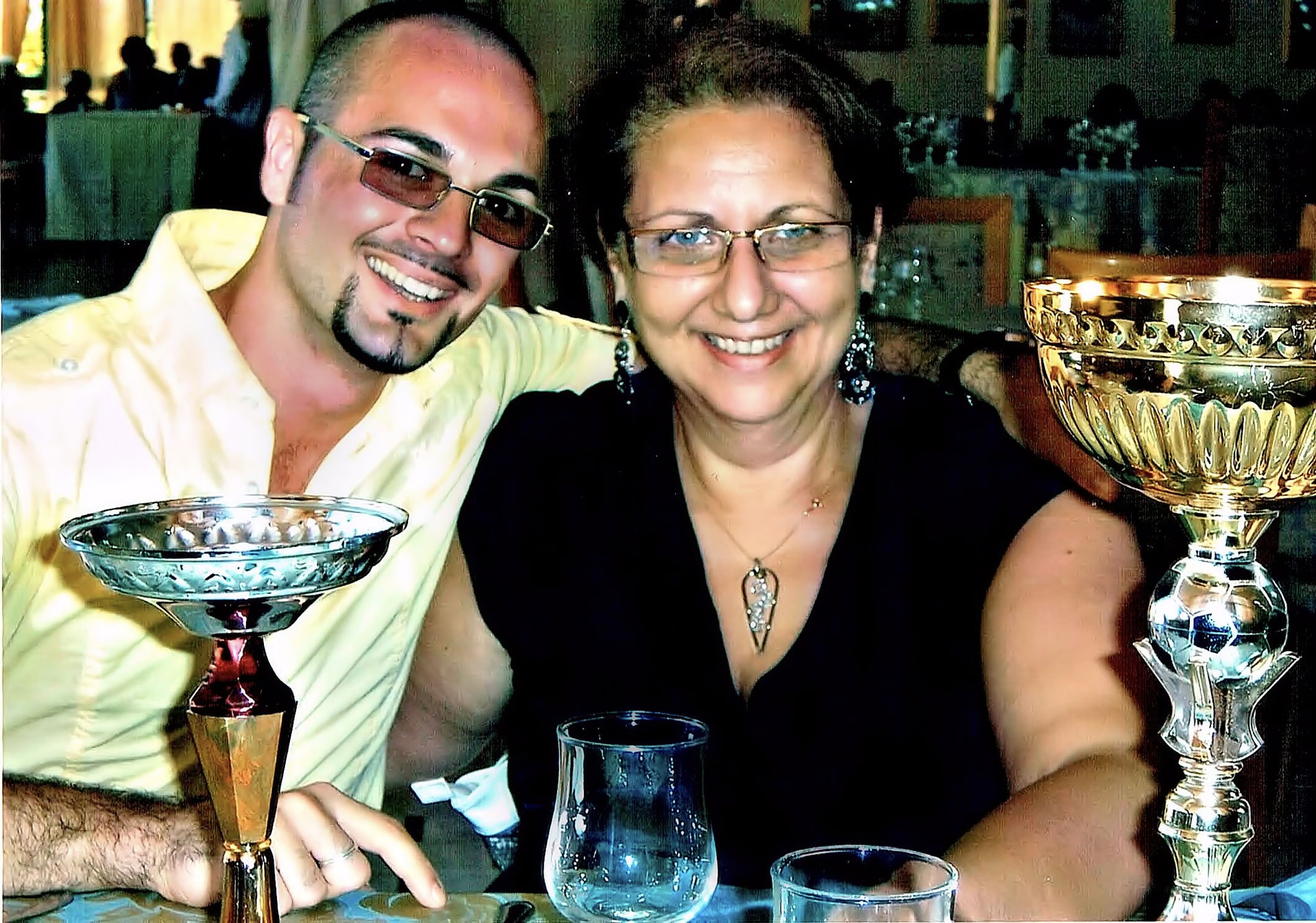 Davide Cristofaro und die Künstlerin Amalia lächelnd am Tisch, zwischen zwei Pokalen