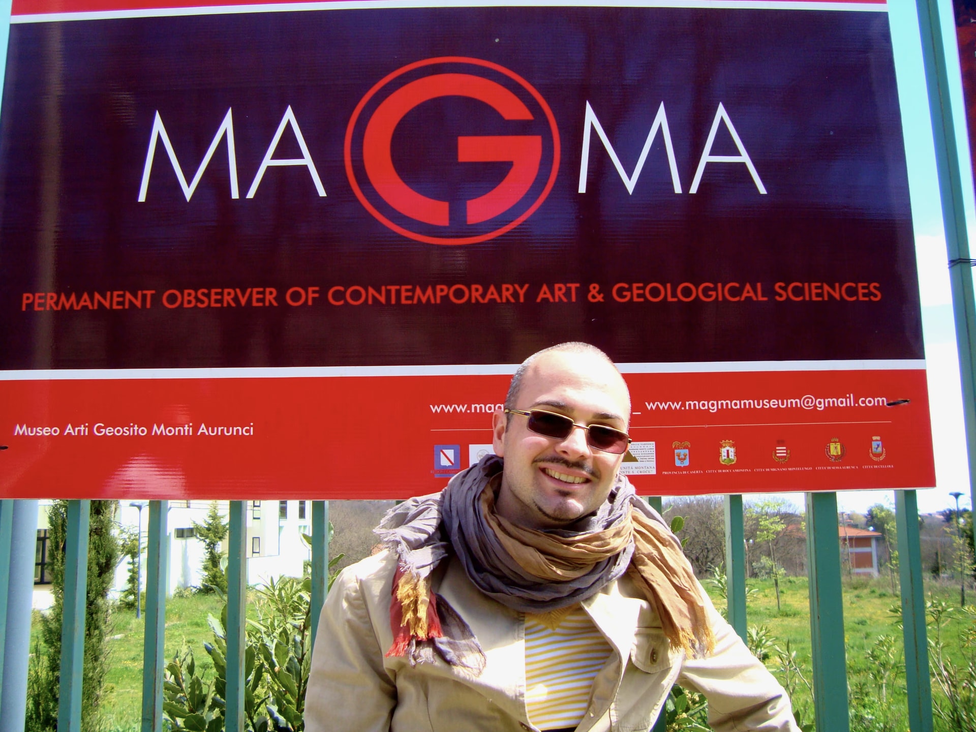 Davide Cristofaro con gafas de sol y bufanda ante el letrero rojo del Museo MAGMA de Roccamonfina