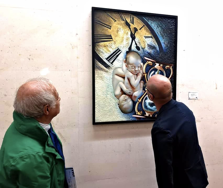 Deux visiteurs s’approchent du Long Écoulement du Temps pour regarder de près les nouveau-nés et le sablier