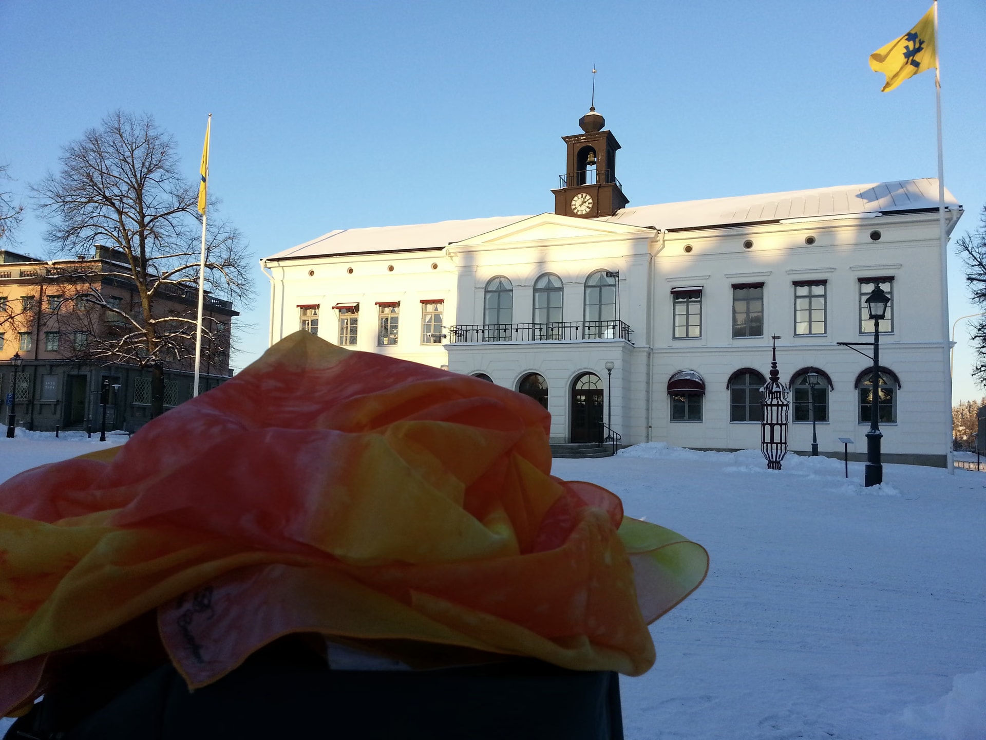 Das handbemalte orange-gelbe Seidentuch von Davide Cristofaro auf dem verschneiten Platz von Köping, vor Kirche und Rathaus