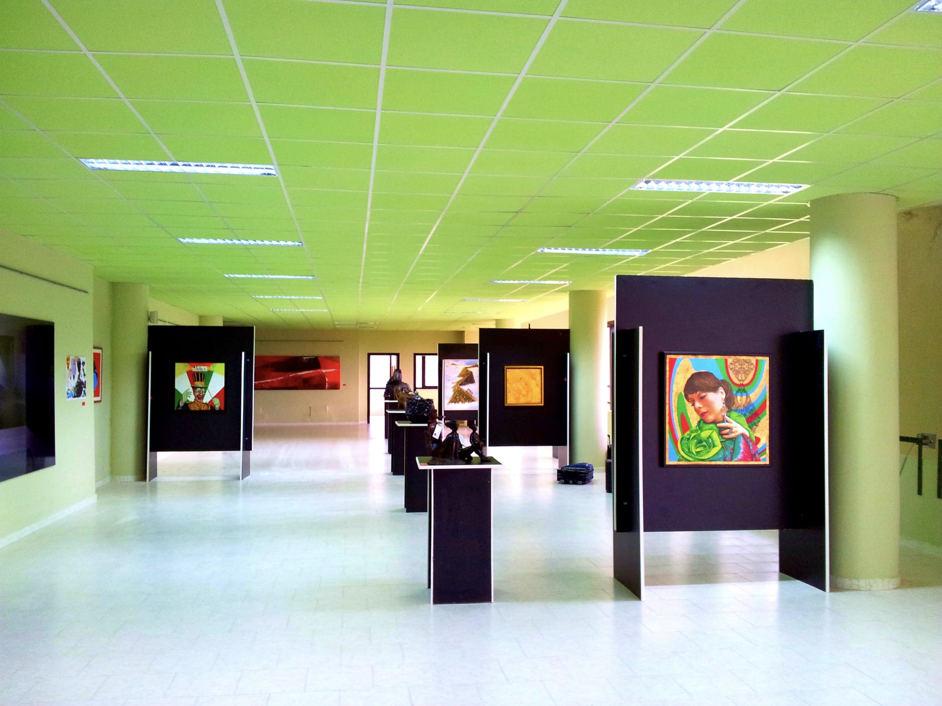 La sala del Museo MAGMA con las tres obras de Davide Cristofaro sobre los paneles negros: Le Cirque a la izquierda, Genesi Solare en el centro y el retrato Morena en primer plano