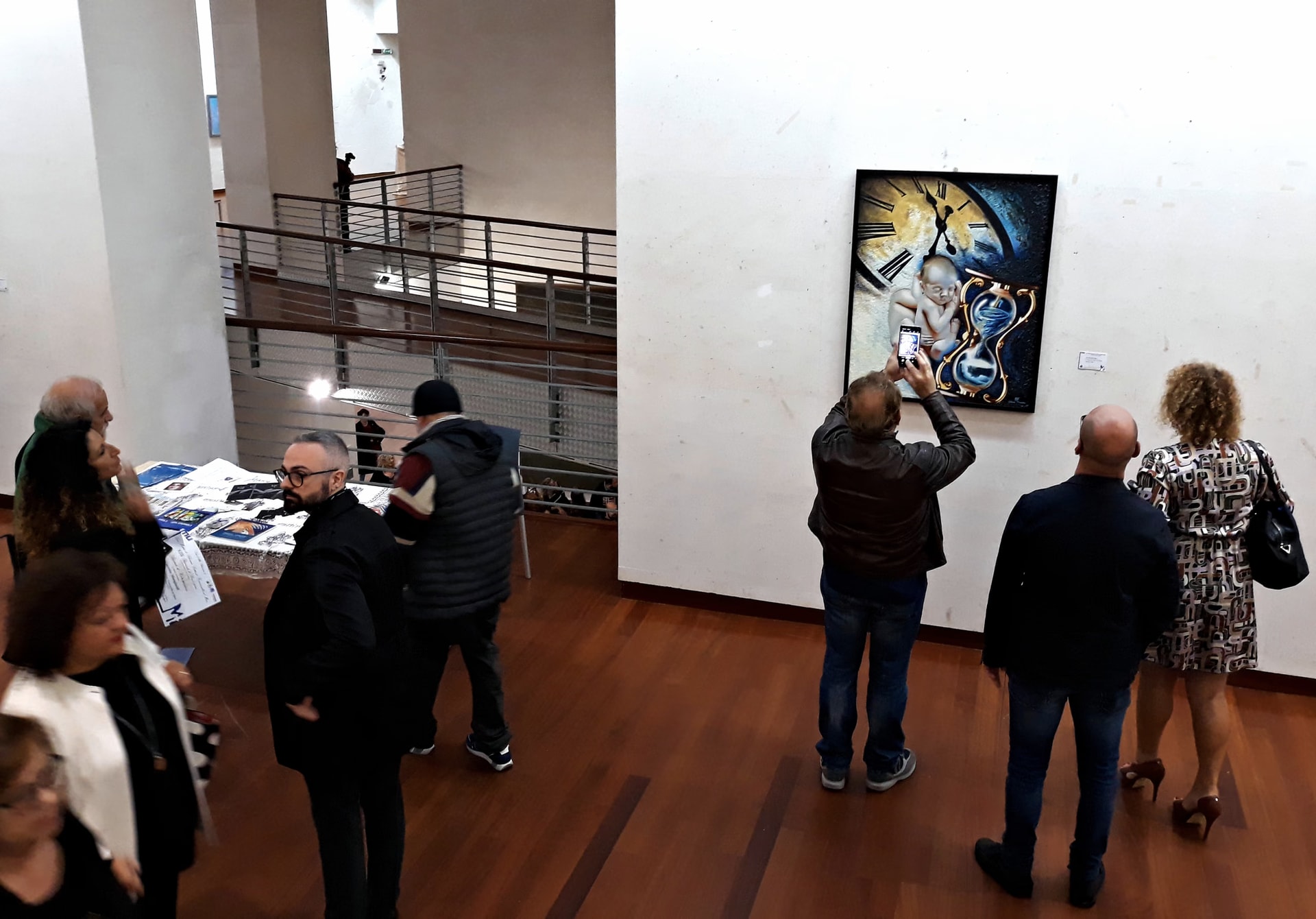Vus depuis la galerie, des visiteurs autour du Long Écoulement du Temps ; l’un d’eux le photographie
