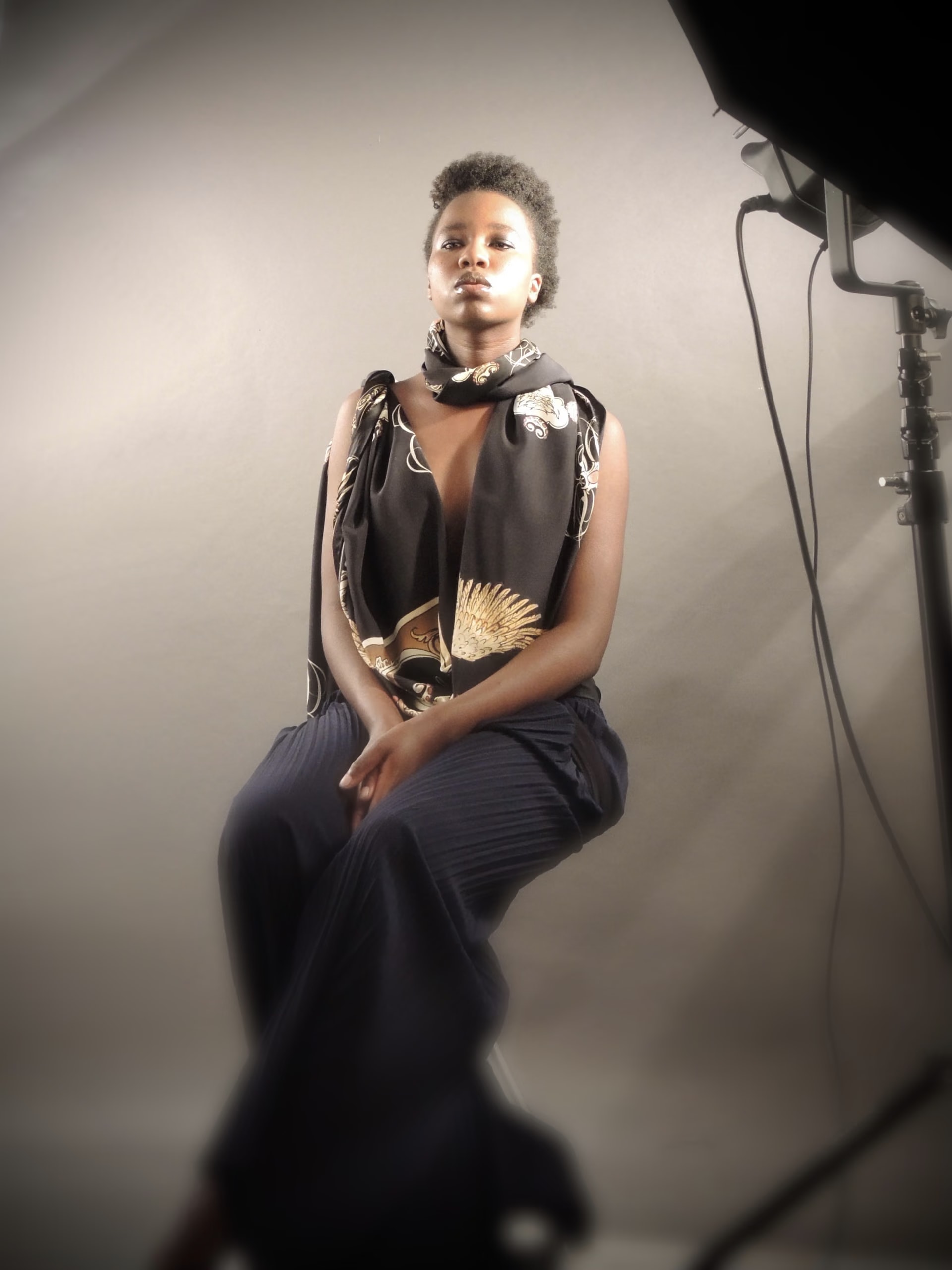 Backstage: Esther Ngumo in posa sul set fotografico con il foulard di seta nero e oro Davide Cristofaro, con la luce da studio a destra