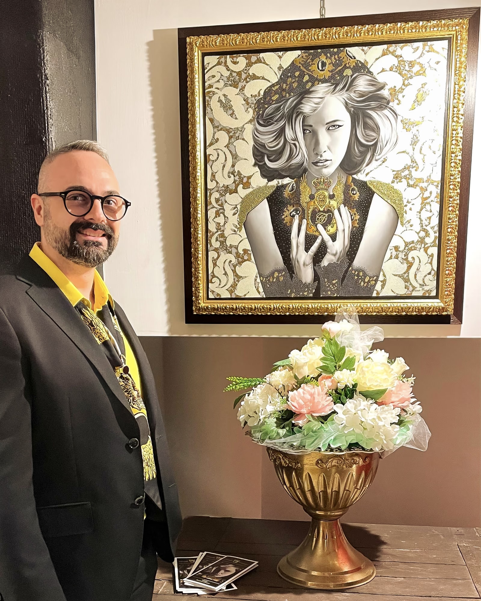 Davide Cristofaro neben Inkar im goldenen Rahmen, auf dem Tisch eine Vase mit Blumen