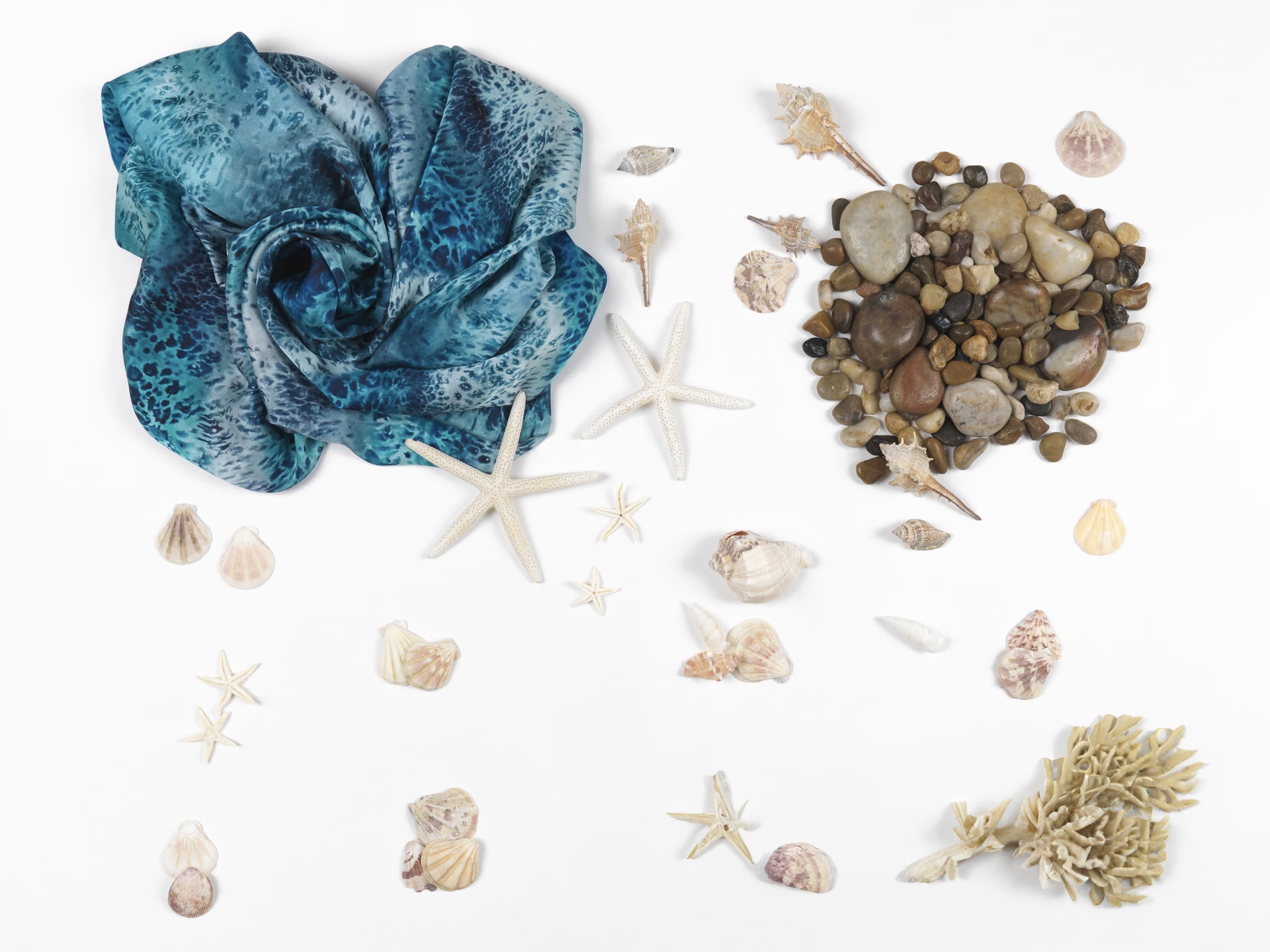 Foulard Deep Blue nei toni dell’azzurro e del blu drappeggiato accanto a stelle marine, conchiglie e ciottoli