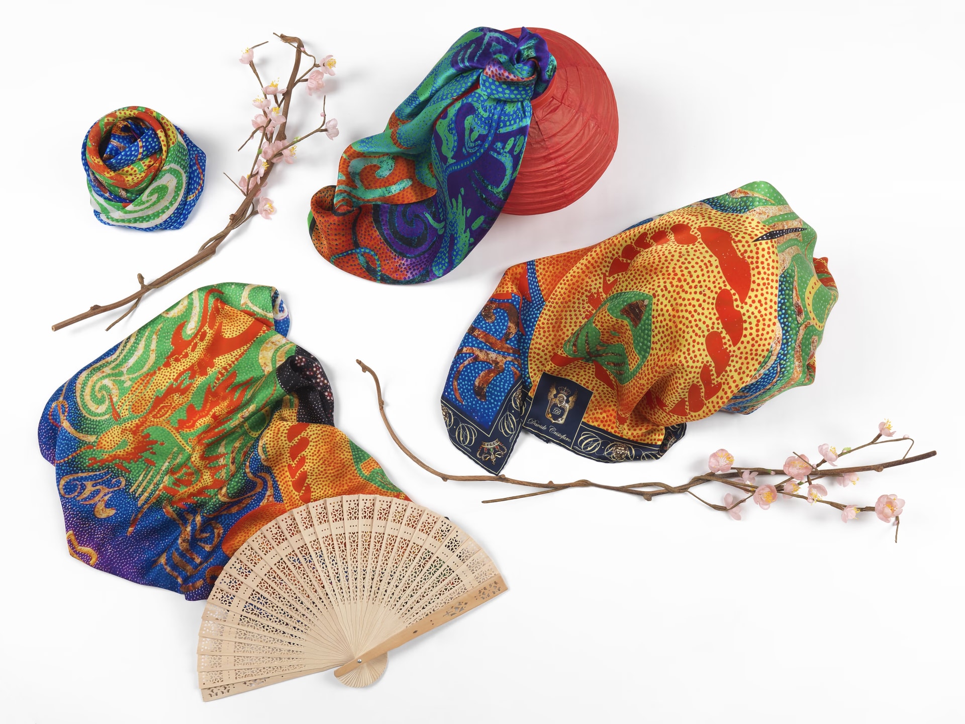 Foulard Dragon nei toni arancio, verde e blu fra un ventaglio di legno traforato, una lanterna rossa e rami di pesco in fiore