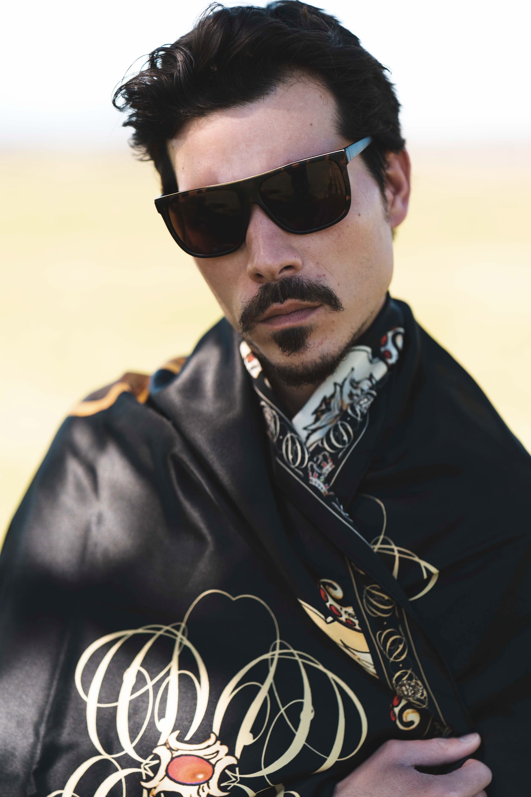 Primo piano di Guglielmo Giovannoni con occhiali da sole e un foulard di seta nero con monogramma dorato sulle spalle