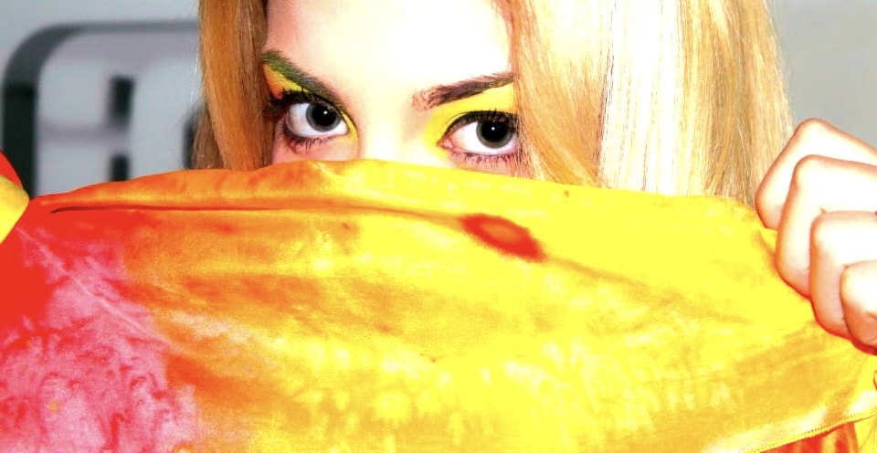 Modella con trucco giallo e verde sugli occhi che copre il viso con un foulard di seta giallo e rosso