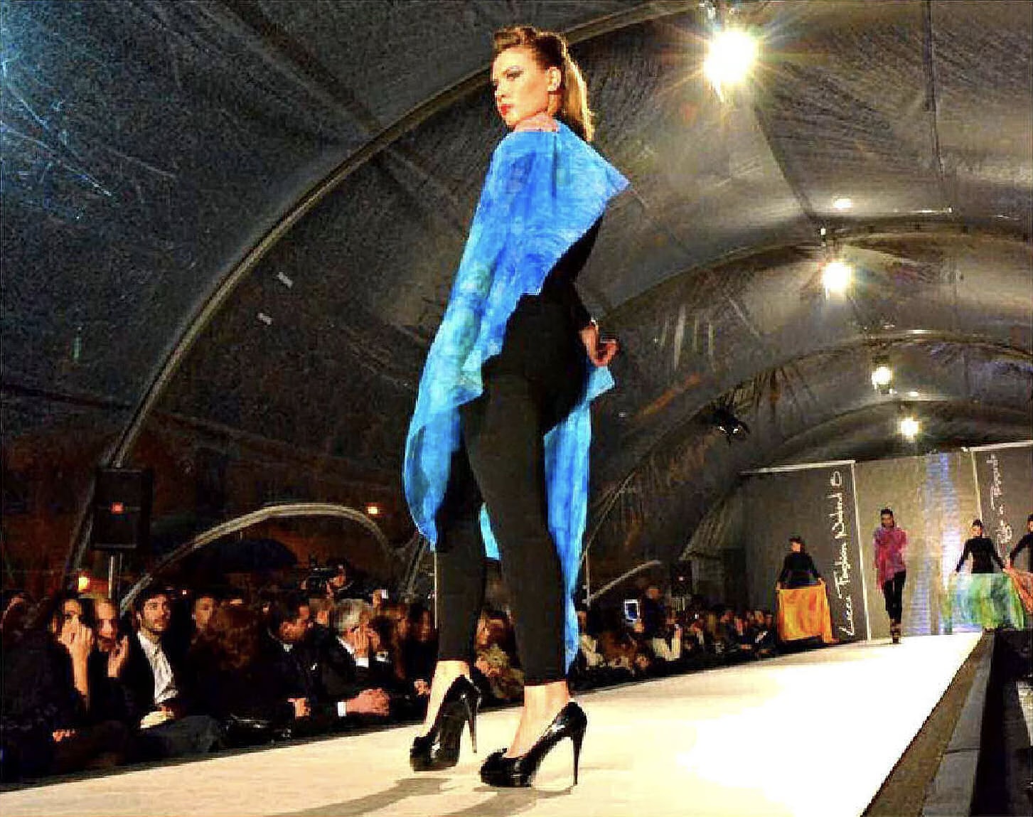 Modella in passerella al Lecce Fashion Weekend 8 con un foulard di seta azzurro dipinto a mano sulle spalle