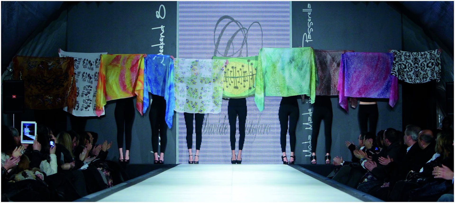 Modelle in fila in fondo alla passerella del Lecce Fashion Weekend 8 reggono le sete dipinte a mano davanti al pubblico