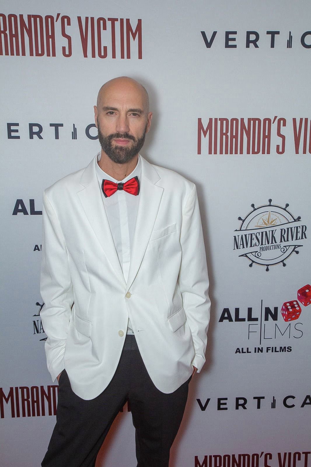 Raimondo Rossi con giacca bianca e papillon rosso Davide Cristofaro davanti al pannello della prima di Miranda’s Victim